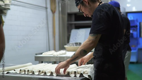 tattooed baker kneading bread doughs and placing the doughs with flour on the workbench of the bread workshop