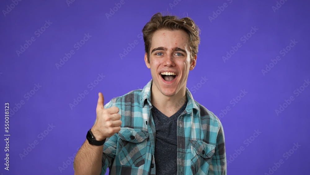 Portrait of amazed young man 20s shocked giving thumbs up. Handsome guy surprised isolated on solid purple background. Portrait of amazed young man 20s shocked giving thumbs up. Handsome guy surprised isolated on solid purple background.