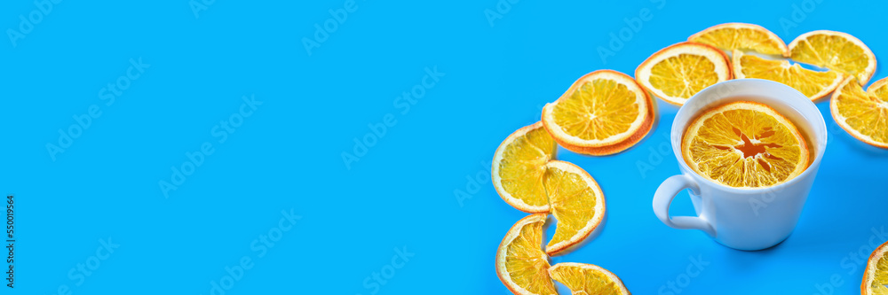 Circle of dried oranges with mug of tea on blue background. Banner. Circle of dried oranges with mug of tea on blue background. Banner.