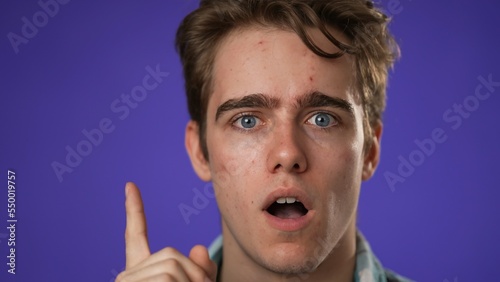 Closeup portrait of thinking, smart puzzled pensive young hipster man 20s thinks comes up with ideas raised finger thumbs up isolated on purple background studio © Robert Peak