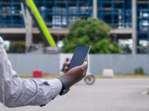 Jeune homme africain tenant un smartphone sur un chantier de construction photo