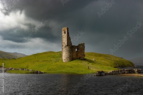 Scenic view of Ardvreck Castle on a green hill against a lake on a cloudy day in Sutherland,Scotland photo