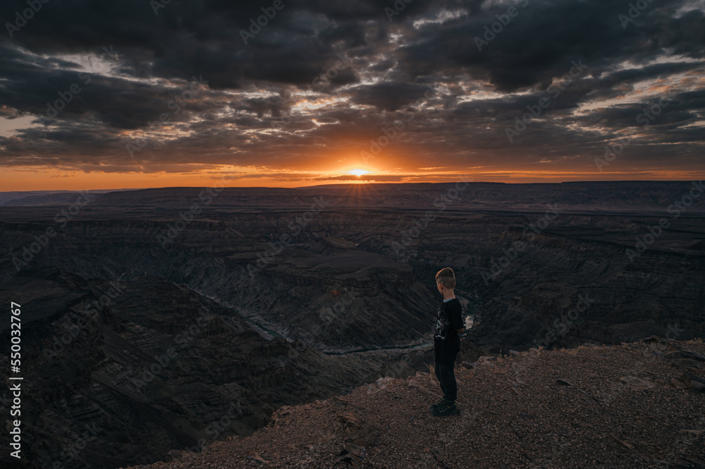 Kleiner Junge schaut in den Fish River Canyon bei Sonnenuntergang (Hobas, Namibia)