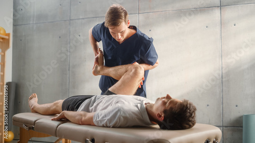 Advanced Sport Physiotherapy Specialist Stretching and Working on Muscle Groups or Joints with Young Male Athlete. Fit Sportsman Recovering from Mild Injury, Undergoing Rehabilitation. photo
