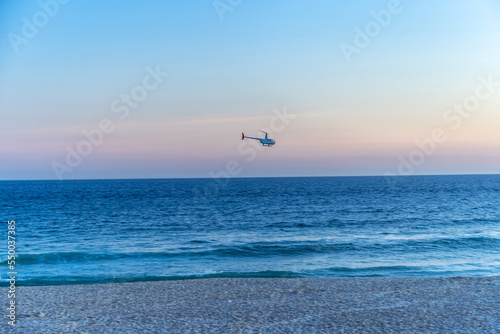 a helicopter flies over the ocean near a sandy beach