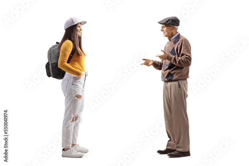 Full length profile shot of a female student with a backpack listening to an elderly man talking