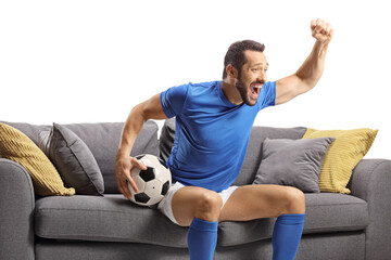 Football player sitting on a sofa holding a ball and watching a match