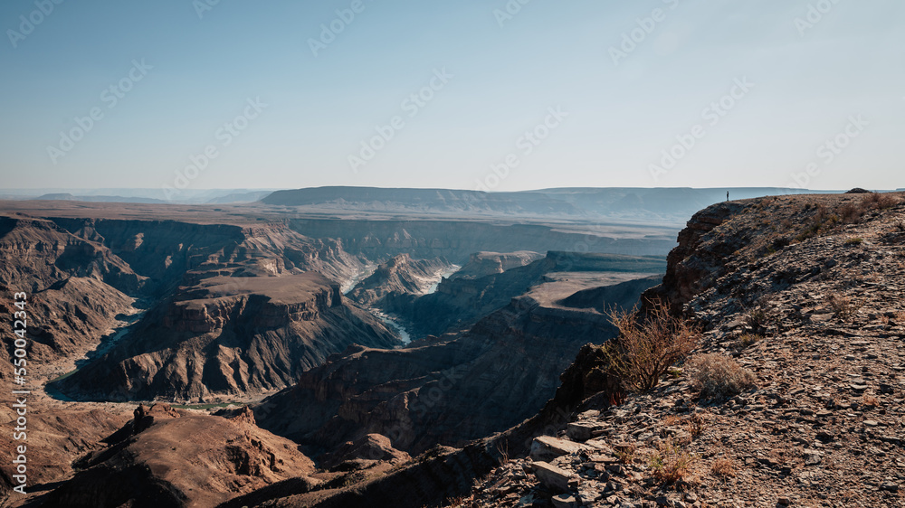 Blick in die unglaubliche Tiefe und Weite des Fich River Canyons in Namibia - am rechten Rand ist ganz klein eine Touristin im Gegenlicht zu erkennen