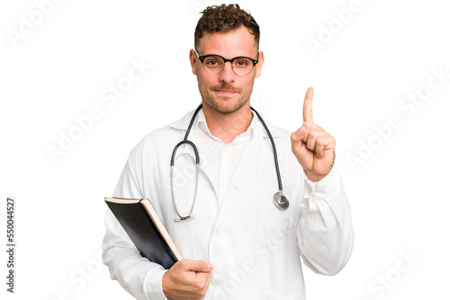 Young doctor caucasian man holding a book isolated showing number one with finger.