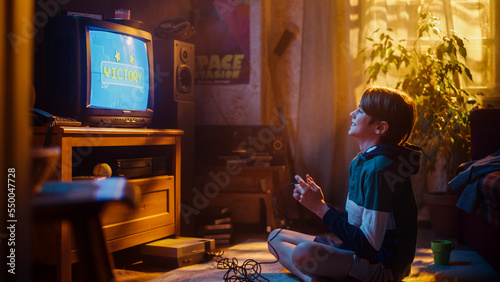 Young Boy Playing Eighties 2D Arcade Space Shooter Game on a Gaming Console at Home in His Room with Old-School Interior. Child Successfully Wins Level. Nostalgic Retro Childhood Concept. © Gorodenkoff