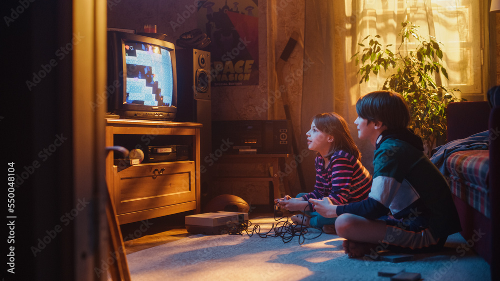 Nostalgic and Happy Childhood Concept: Young Brother and Sister Playing 8 Bit 2D Arcade Video Game on a Retro TV Set at Home in a Room with Period-Correct Interior. Friends Completing the Level.