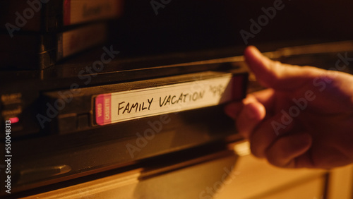 Close Up of a Person Inserting a VHS Cassette in a Player with Happy and Nostalgic Vacation Footage from Home Video Camera. Retro Nineties Technology. Old VCR with Shallow Depth of Field and Bokeh. photo