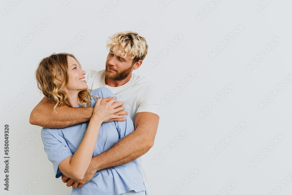 Young cheerful couple hugging while standing isolated over white wall Young cheerful couple hugging while standing isolated over white wall