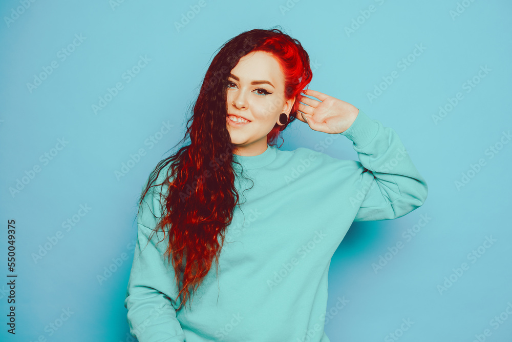 Woman in a blue sweater on a blue background posing. A beautiful brunette with long hair and and tunnels in her ears. Eyeliner and trendy makeup. Woman in a blue sweater on a blue background posing. A beautiful brunette with long hair and and tunnels in her ears. Eyeliner and trendy makeup.