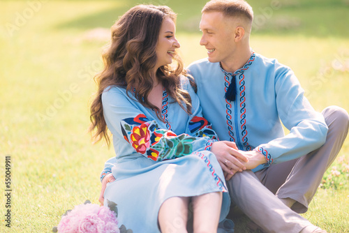 A beautiful bride in a blue dress hugs a stylish smiling groom in a shirt, sitting on green grass. newlyweds in love.