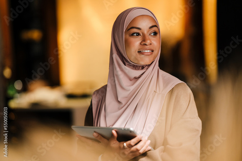 Fotografering Arabian woman working on tablet while standing indoors