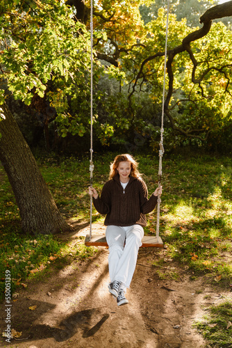Young woman swinging on wooden swing in park