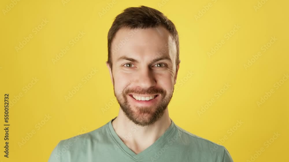 Cute bearded man smiling and looking at camera over yellow background. Handsome happy guy. Positive emotions. Close-up in 4K, UHD Cute bearded man smiling and looking at camera over yellow background. Handsome happy guy. Positive emotions. Close-up in 4K, UHD
