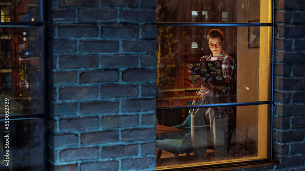 Creative Professional Woman Working from Home in Stylish Living Room. Female Standing by the Window, Browsing Internet, Checking Social Media and Corporate Email Inbox. View Through the Window. Creative Professional Woman Working from Home in Stylish Living Room. Female Standing by the Window, Browsing Internet, Checking Social Media and Corporate Email Inbox. View Through the Window.