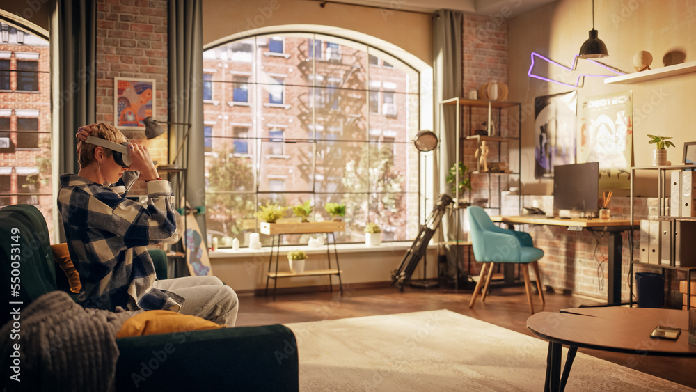 Young Creative Female Sitting on a Couch in Loft Stylish Living Room and Holding New VR Headset in Hands. Beautiful Woman is About to Enter Digital Metaverse World to Play With Her Friends.