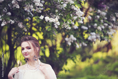 Beautiful fair-haired girl in a vintage look, in a spring park near a lush white lilac bush