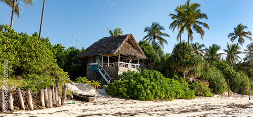 Am Strand der Matemwe Beach auf der Insel Sansibar. Ein traditionelles Holzhaus, ein Fischerboot und Palmen auf der karibischen Insel und ein blauer Himmel, Panorama.