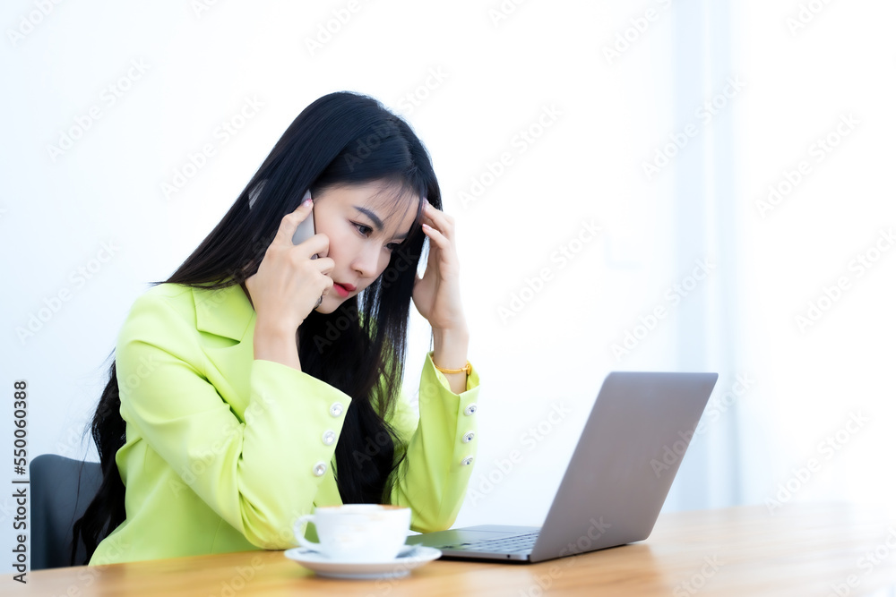 Young business woman wears green suit using laptop computer and mobile phone. Beautiful woman talking on the phone feeling sad and moody. Business woman looking irritable while talking on the phone. Young business woman wears green suit using laptop computer and mobile phone. Beautiful woman talking on the phone feeling sad and moody. Business woman looking irritable while talking on the phone.