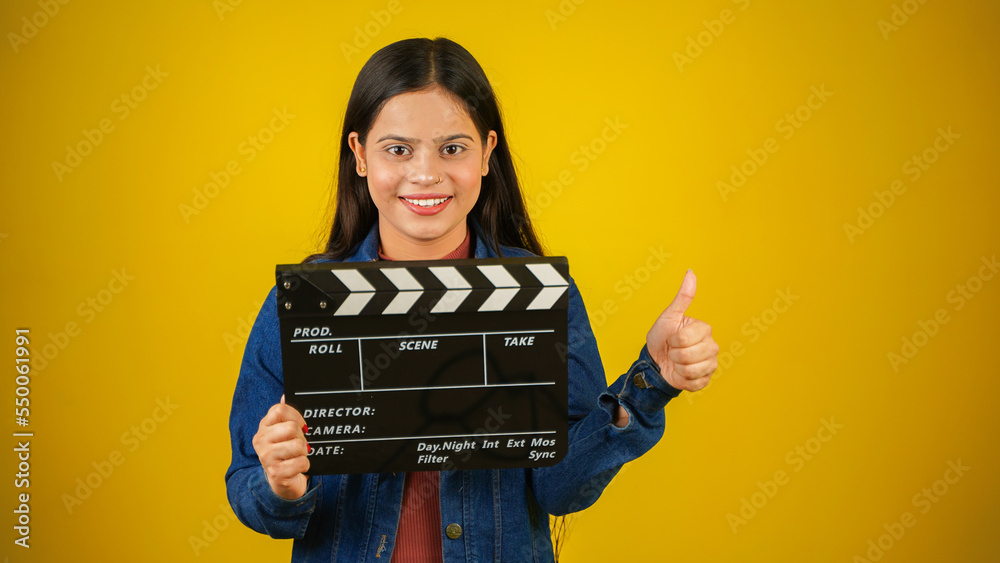 Beautiful young Asian Indian woman standing holding clapperboard saying nice, clapper board used in film making, isolated on color background studio portrait