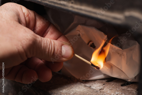 Hand of a man holding burning match and making fire in the solid fuel boiler. House heating, warmth at home during cold season