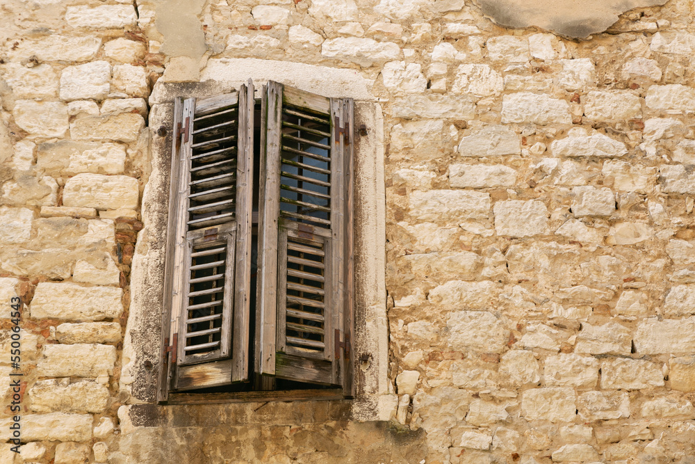 Closed rustic brown wooden window shutters on the background of an old white stone wall. Copy space