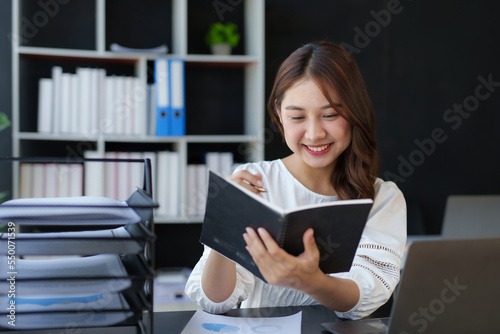 Beautiful Asian businesswoman working on paperwork at her desk in the office review work from different department, take minute of meetings report other document.