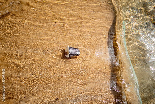 Vaso de papel tirado en las aguas de la playa de la ciudad de benidorm sin reciclar mientras el mar se lo lleva a sus profundidades. photo