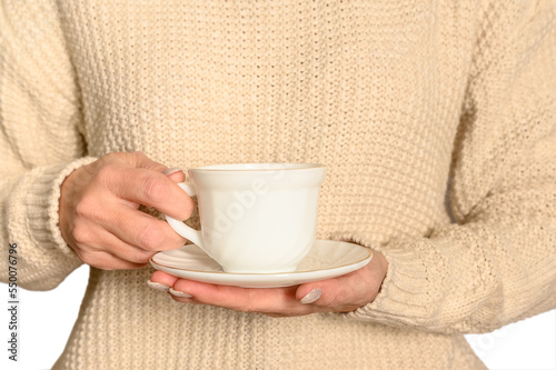 A woman in a white jumper holds a white cup and saucer. Autumn concept.