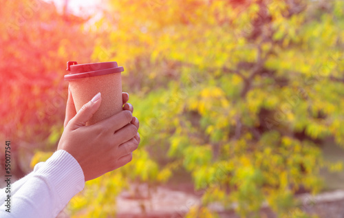 Female hands holding a glass of coffee with yellow leaves background
