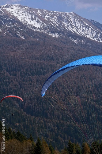 A shot of Two men in paragliders flying in the mountains Winter forest in Trentino-Alto Adige Italy