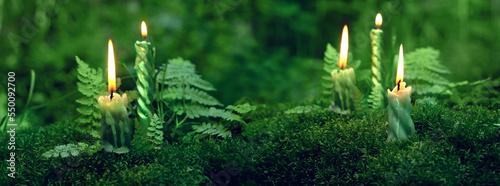 burning candles on moss, dark green blurred natural background. magic candles for witch ritual in forest, mysterious fairy scene. banner