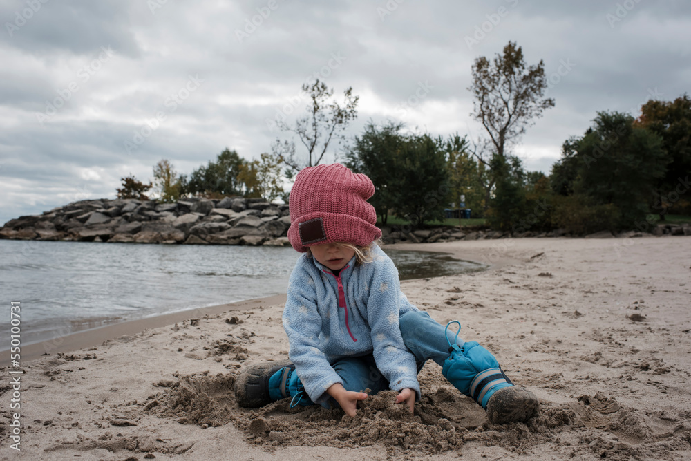 Girl playing with sand while sitting at beach against cloudy sky Girl playing with sand while sitting at beach against cloudy sky