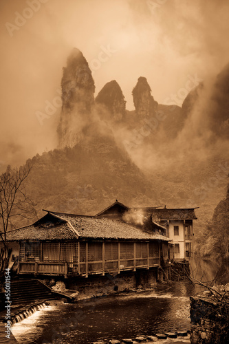 Rock karsts in fog behind a small Chinese village and a stream.  Dehang, Hunan, China. photo