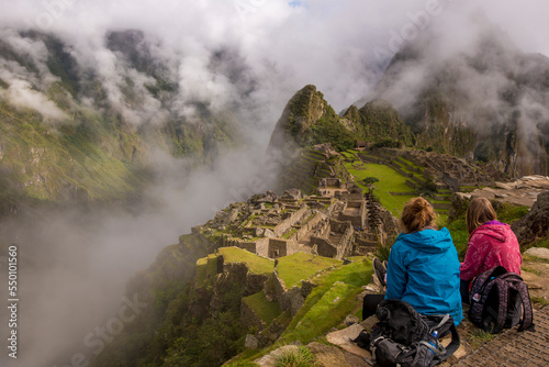 Two young women looking over ruins high in the mountains.   Machu Picchu, Peru.