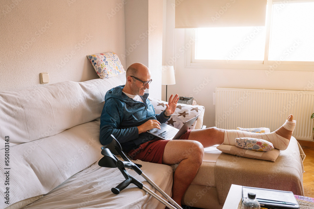 Obraz premium Injured man with bandaged foot using a laptop.