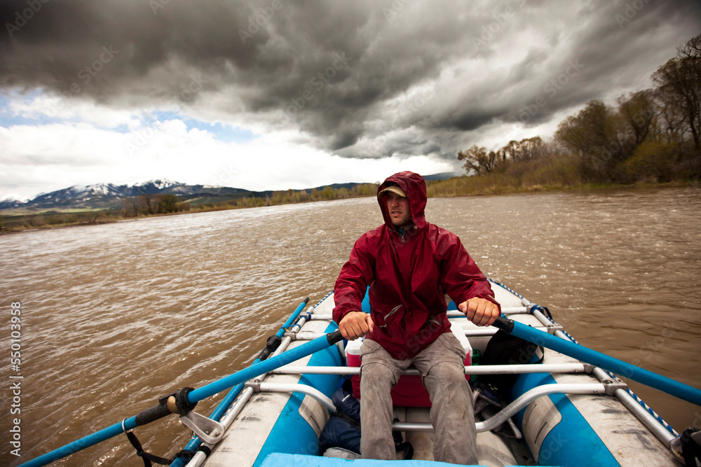 A man rafts down a rive under stormy skies in Montana. A man rafts down a rive under stormy skies in Montana.