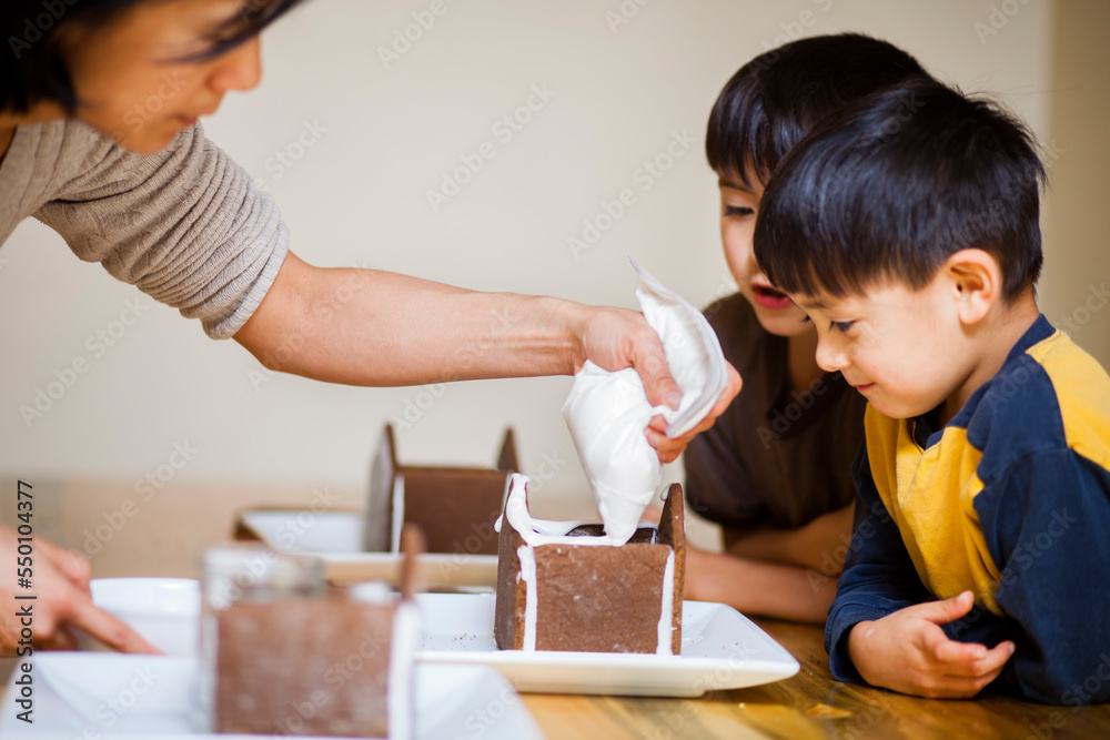 A Japanese American mother helps put together a Gingerbread house at Christmastime with her two Japanese American sons with whom the younger is four years old and the older is is 7 A Japanese American mother helps put together a Gingerbread house at Christmastime with her two Japanese American sons with whom the younger is four years old and the older is is 7
