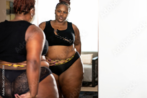 Black woman with braids wearing waitstbeads admiring herself in the mirror