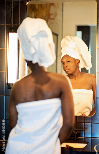 Black woman with towel on her head getting ready in the bathroom mirror