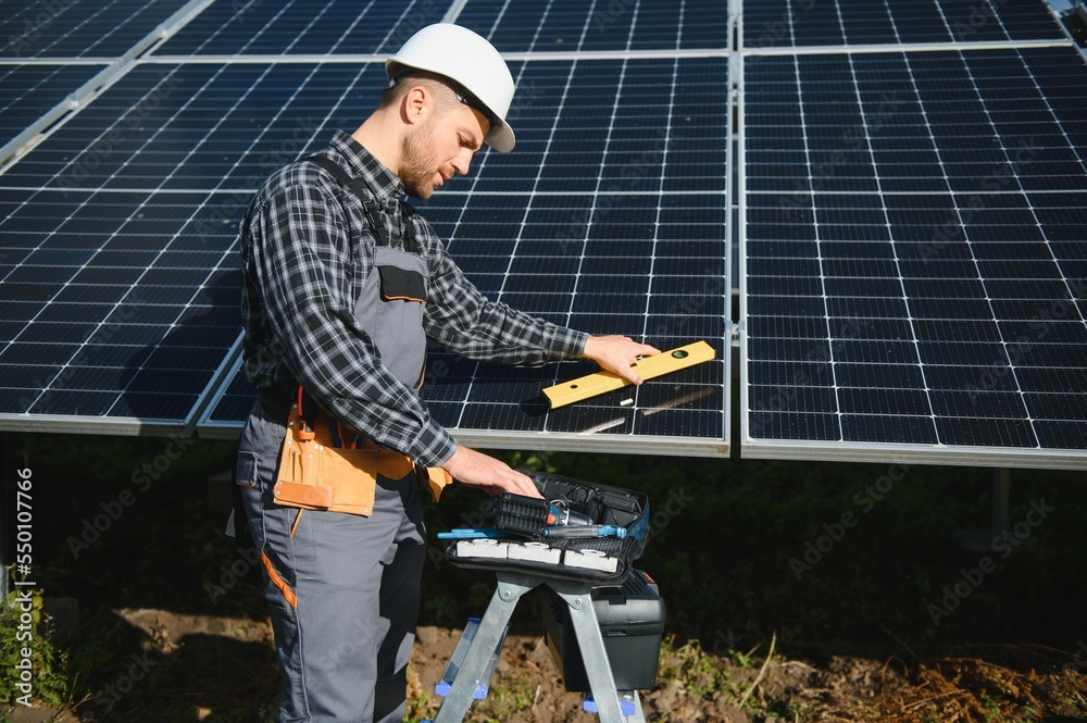 Male worker in uniform outdoors with solar batteries at sunny day. Male worker in uniform outdoors with solar batteries at sunny day.