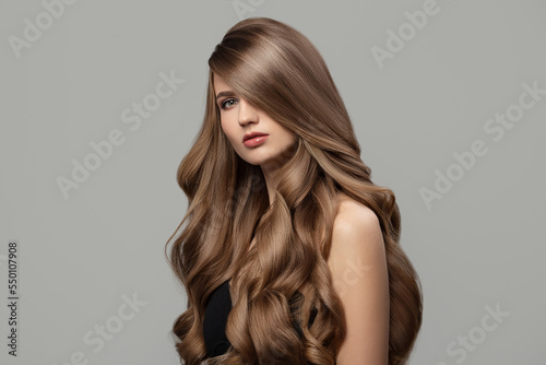 Beautiful woman with long wavy hair. Gray background.