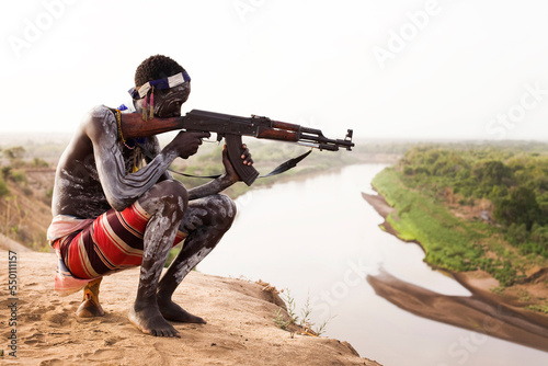 A young man holds his kalashnikov rifle while overlooking the Omo river in the remote Omo Valley of Ethiopia photo