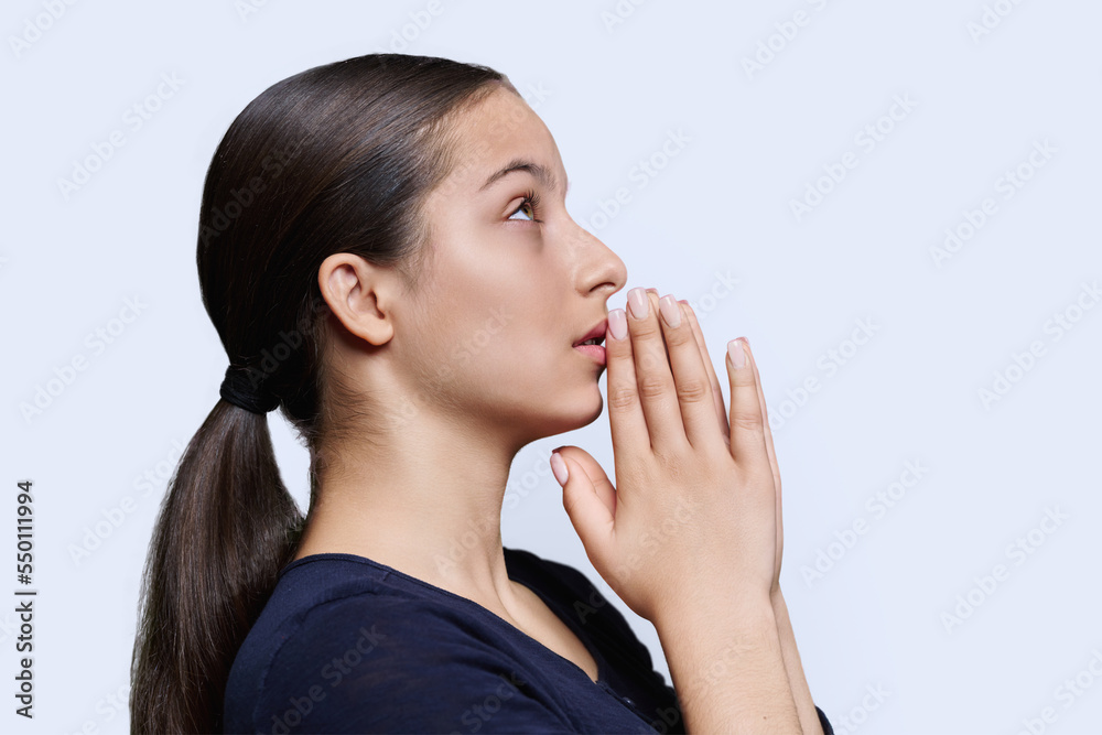 Young female pleading, holding hands in prayer on white background, profile view Young female pleading, holding hands in prayer on white background, profile view