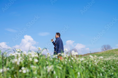 Wallpaper Mural Side view of man standing on a meadow while smelling flowers against blue sky Torontodigital.ca