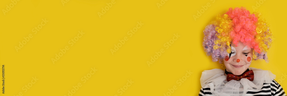 A boy in a clown costume on the background of a bright yellow wall is fooling around and smiling